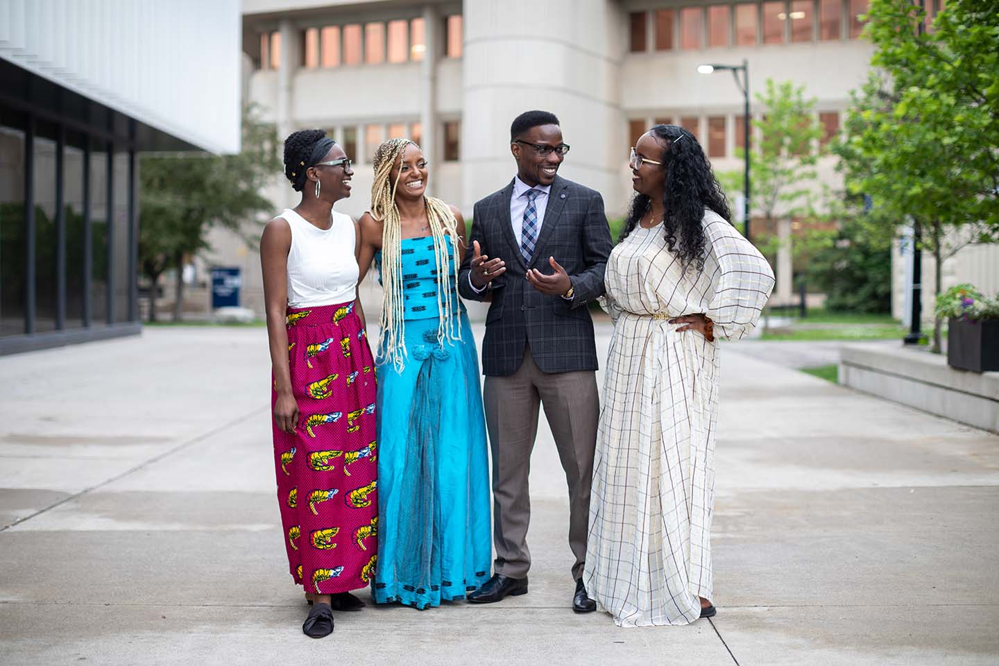 Four students smiling at each other in front of a university building