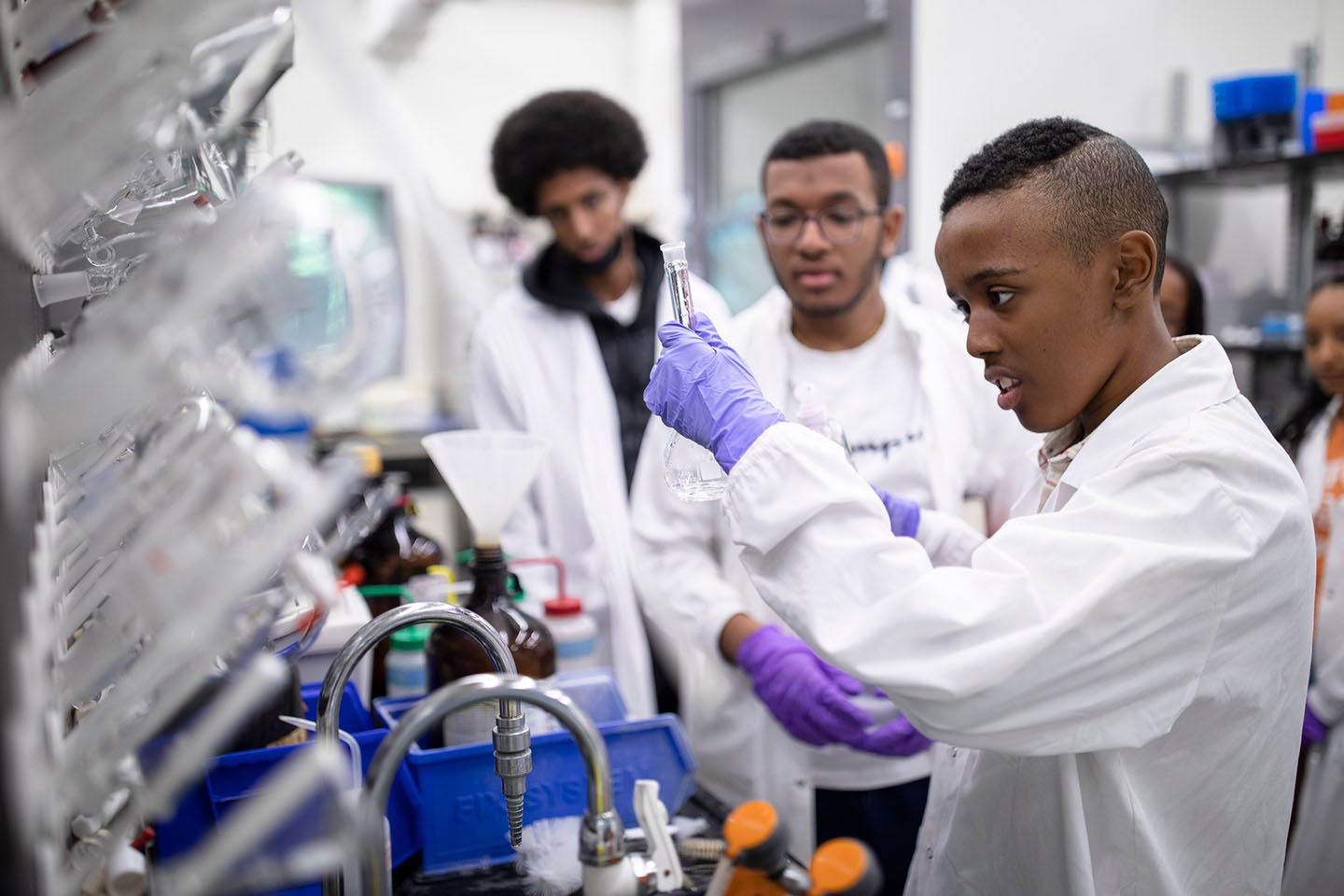 Three students, working in a scientific lab, wearing purple gloves